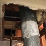 A close-up view of exposed plumbing pipes and a large, insulated duct running vertically within a wall cavity