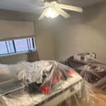 The furniture, including a bed and a dresser, is covered in clear plastic sheeting