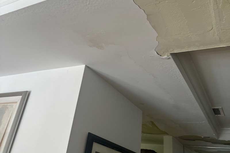 Water-stained ceiling with peeling paint, showing signs of severe water damage and discoloration.