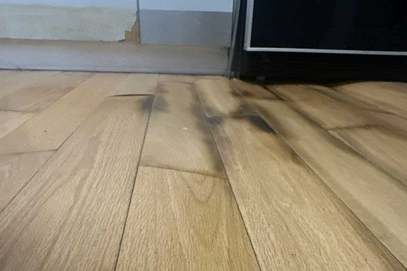 Hardwood floor with dark water stains and swelling, showing moisture damage.